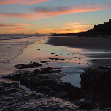 View at dawn of Bamburgh Castle from the beach and rocks, United Kingdom