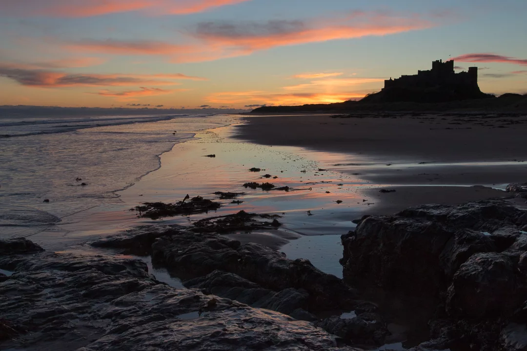 View at dawn of Bamburgh Castle from the beach and rocks, United Kingdom