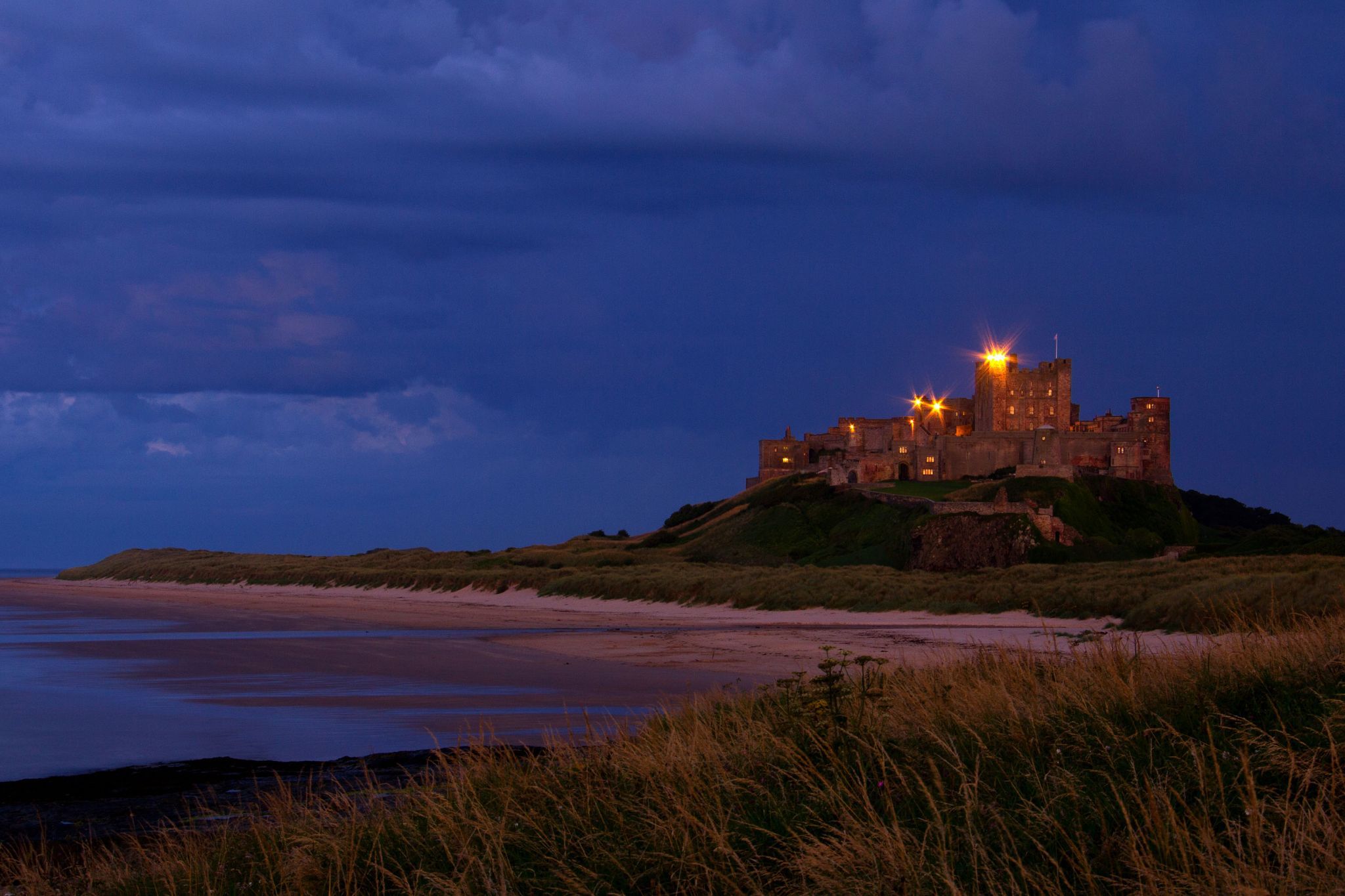 View at dawn of Bamburgh Castle from the beach and rocks, United Kingdom