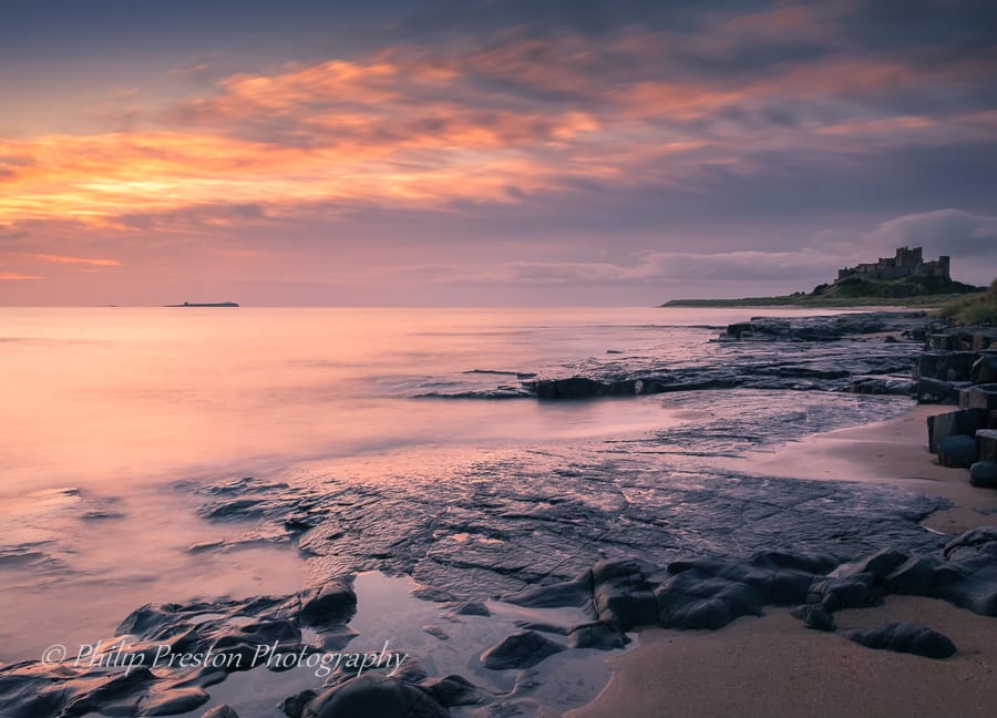View at dawn of Bamburgh Castle from the beach and rocks, United Kingdom