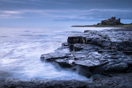 View at dawn of Bamburgh Castle from the beach and rocks